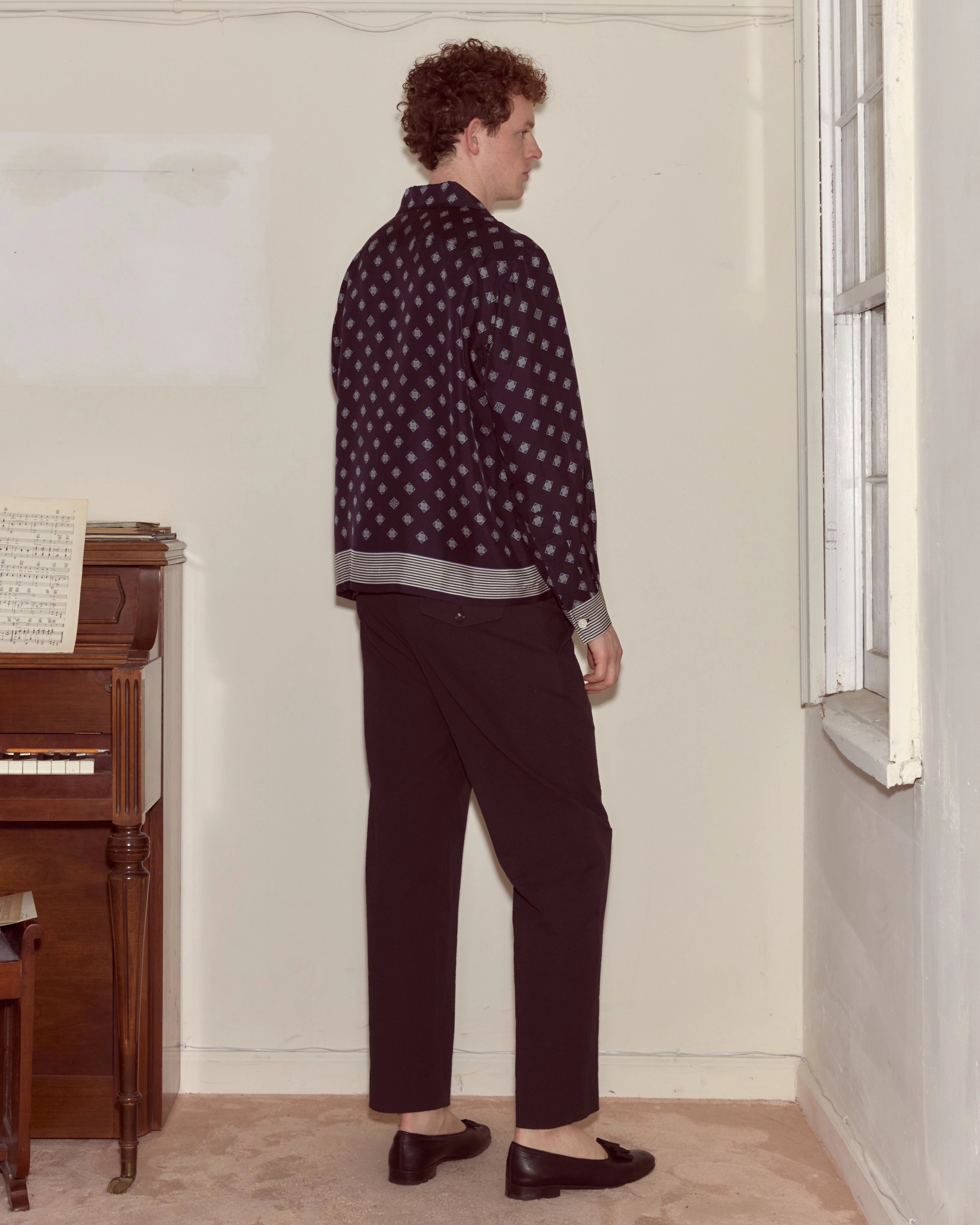 Model wearing navy Bode silk long-sleeve shirt with diamond foulard print and striped trim.