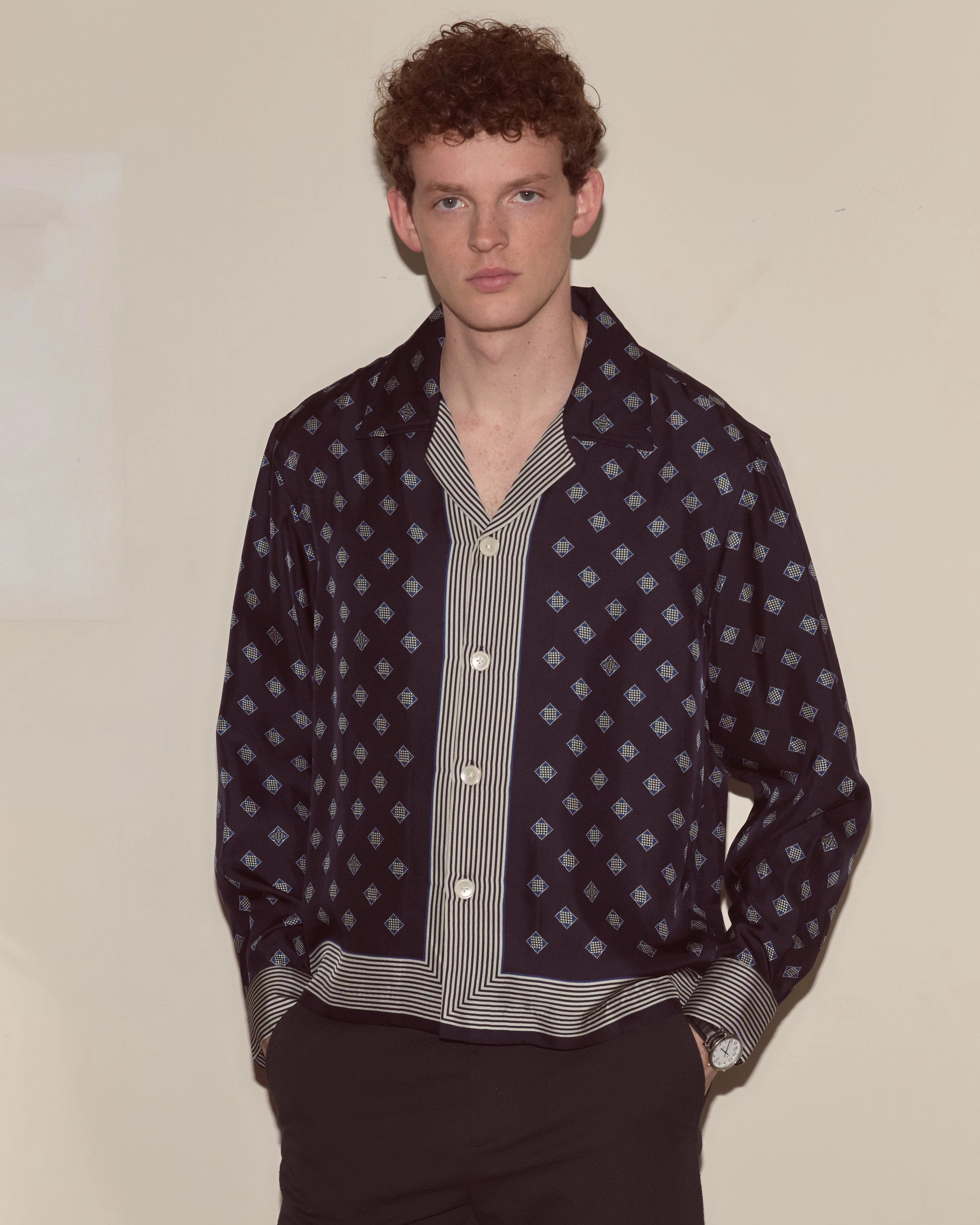 Model wearing navy Bode silk long-sleeve shirt with diamond foulard print and striped trim.