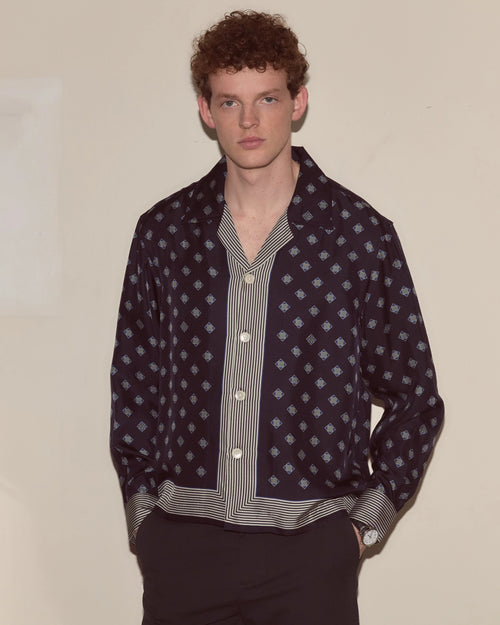 Model wearing navy Bode silk long-sleeve shirt with diamond foulard print and striped trim.