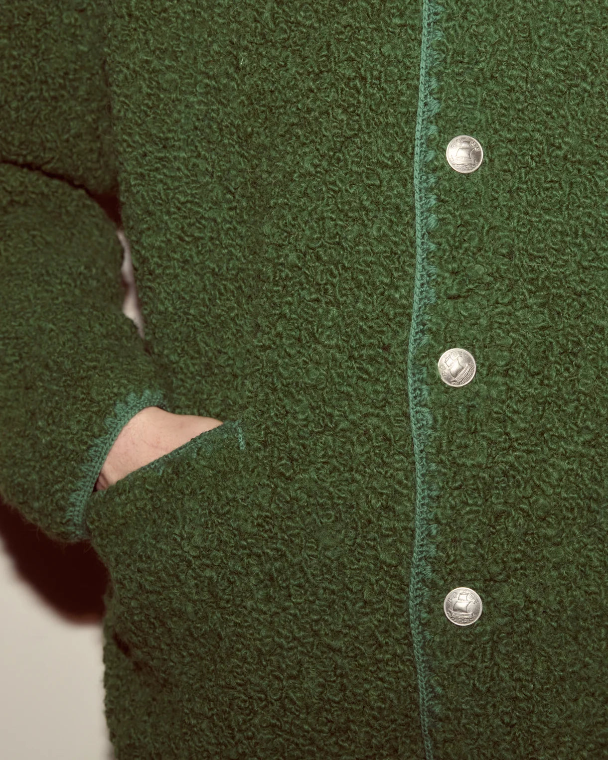 Close-up of a green textured cardigan with silver buttons.