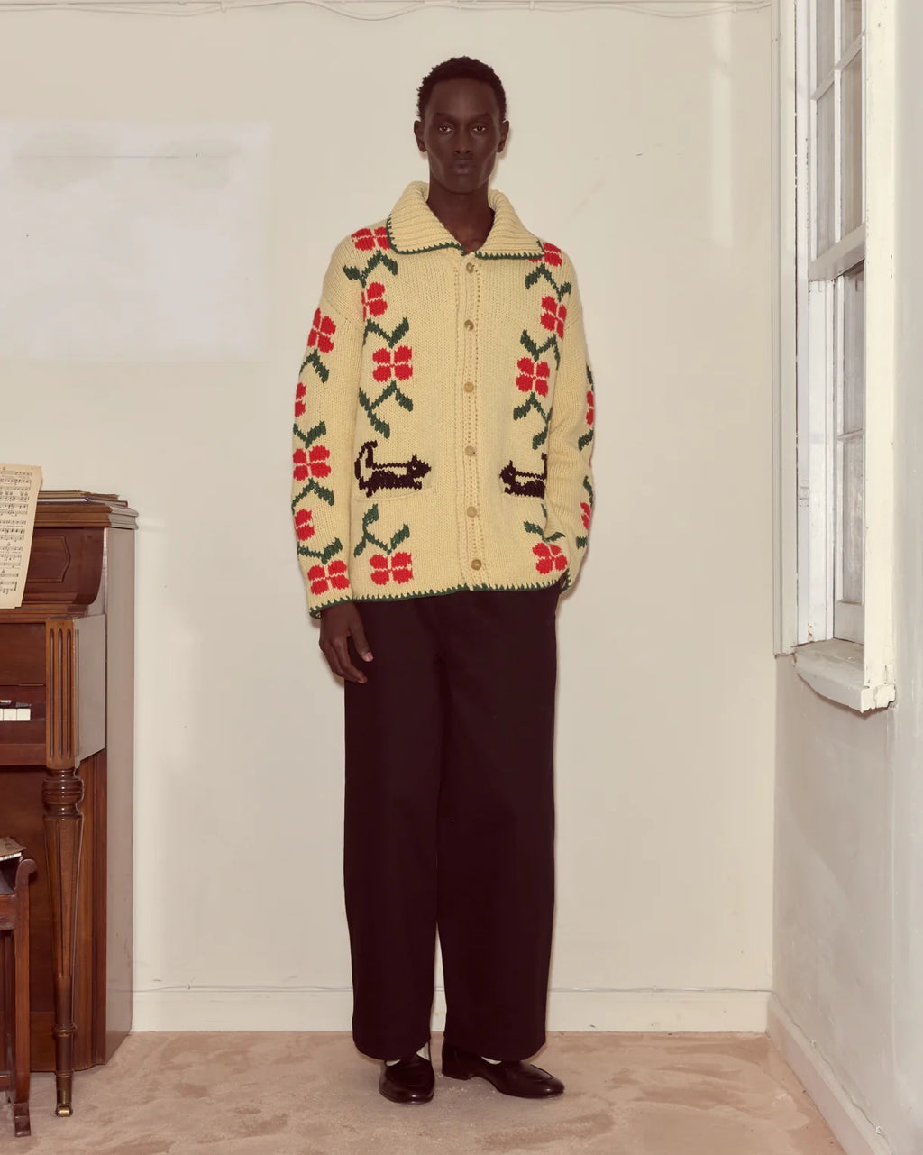 Person wearing a patterned sweater in a room with a window and wooden furniture.