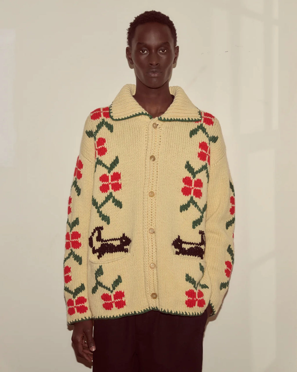 Person wearing a cream-colored sweater with red floral patterns and black accents on a plain background