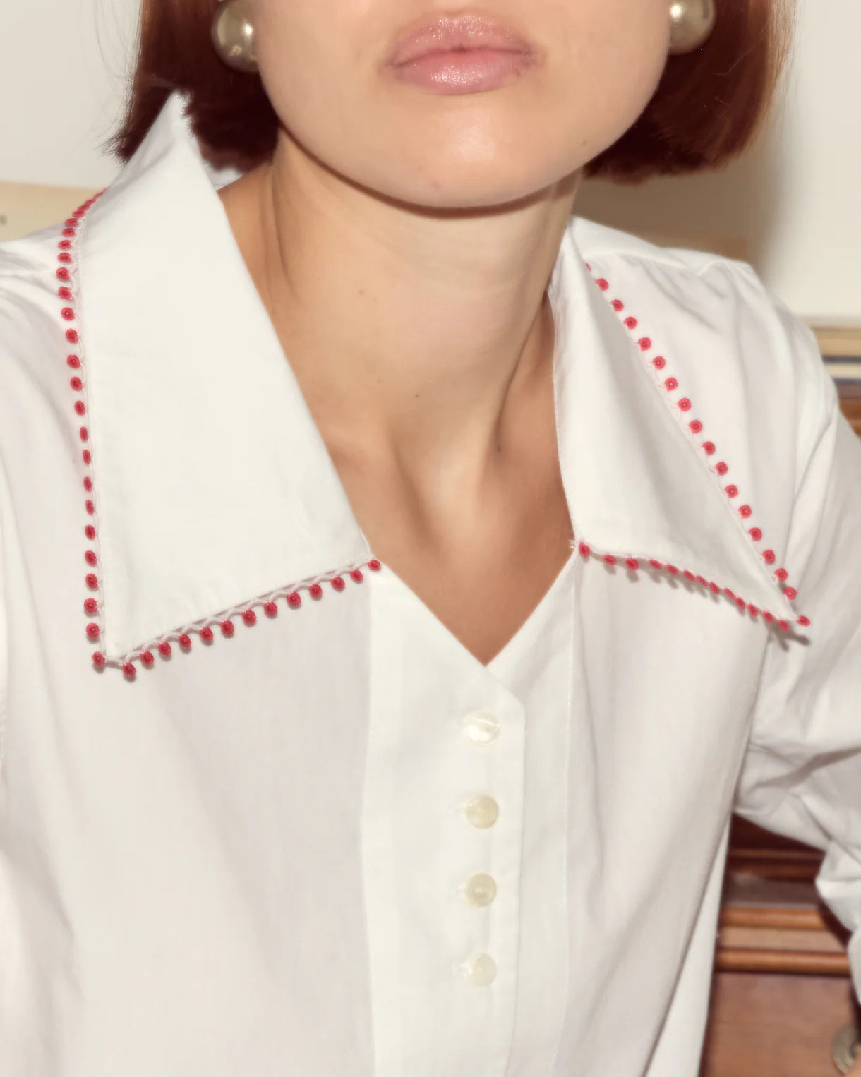 Close-up of a white blouse with red trim worn by a person.