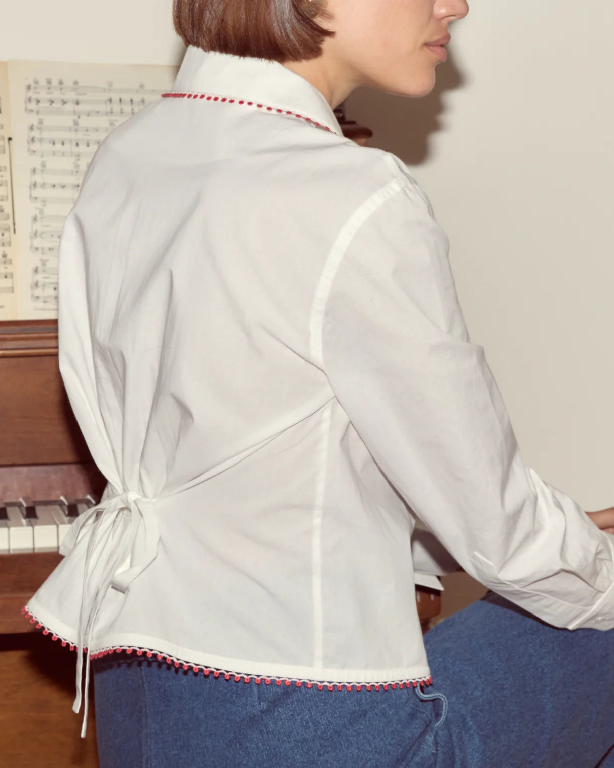 Person wearing a white blouse with red trim sitting in front of a piano