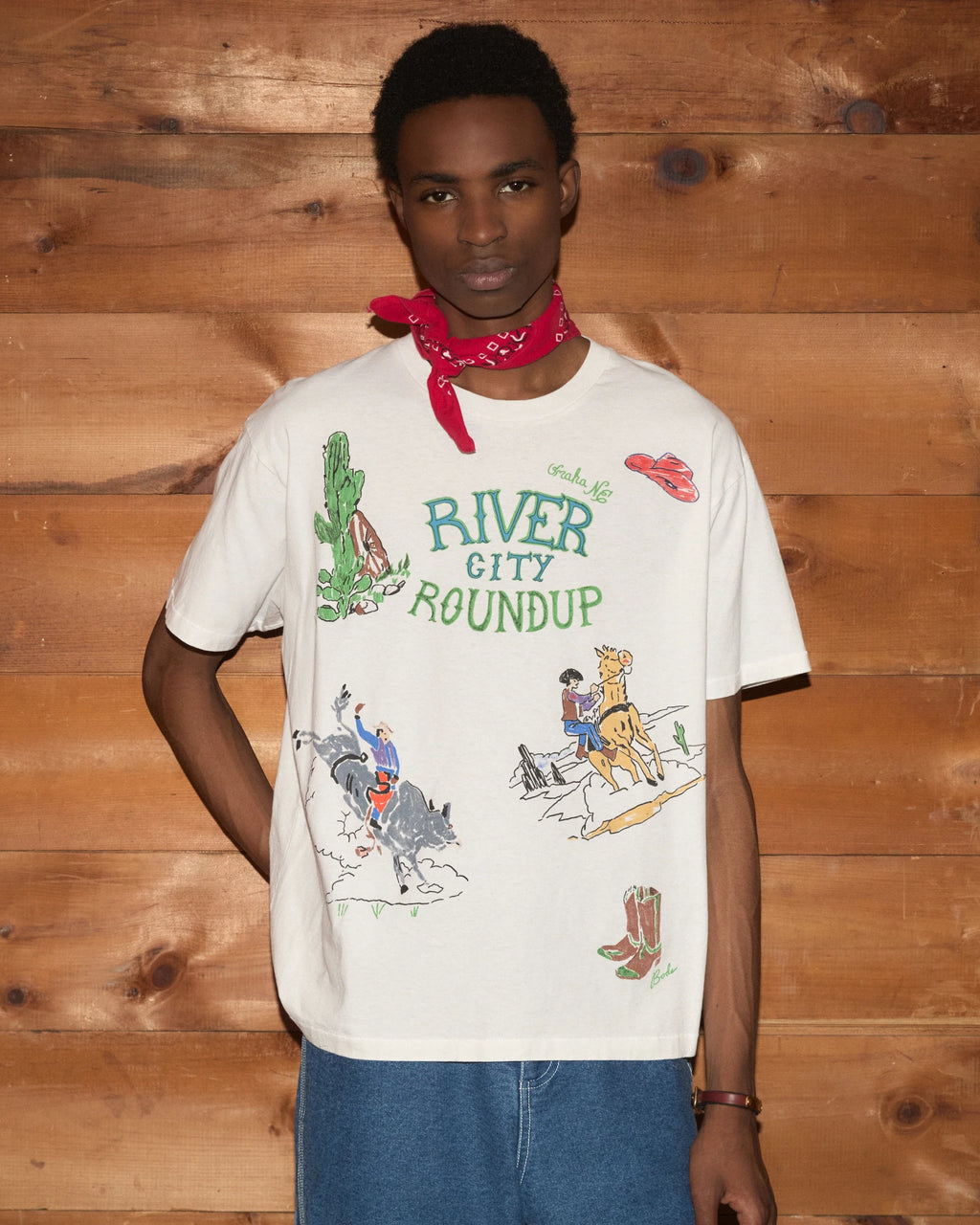 Model wearing Bode River City Tee in white with a colorful River City Roundup graphic and Western-inspired illustrations.