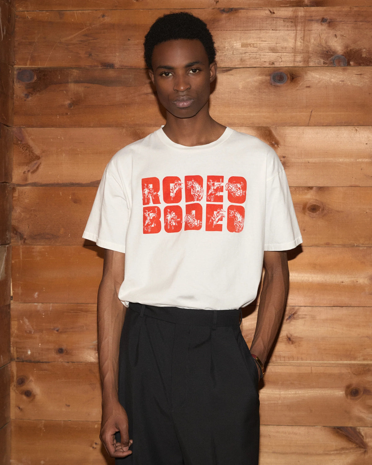 Model wearing Bode Rodeo Bodeo Tee in white with a red flocked graphic across the chest.