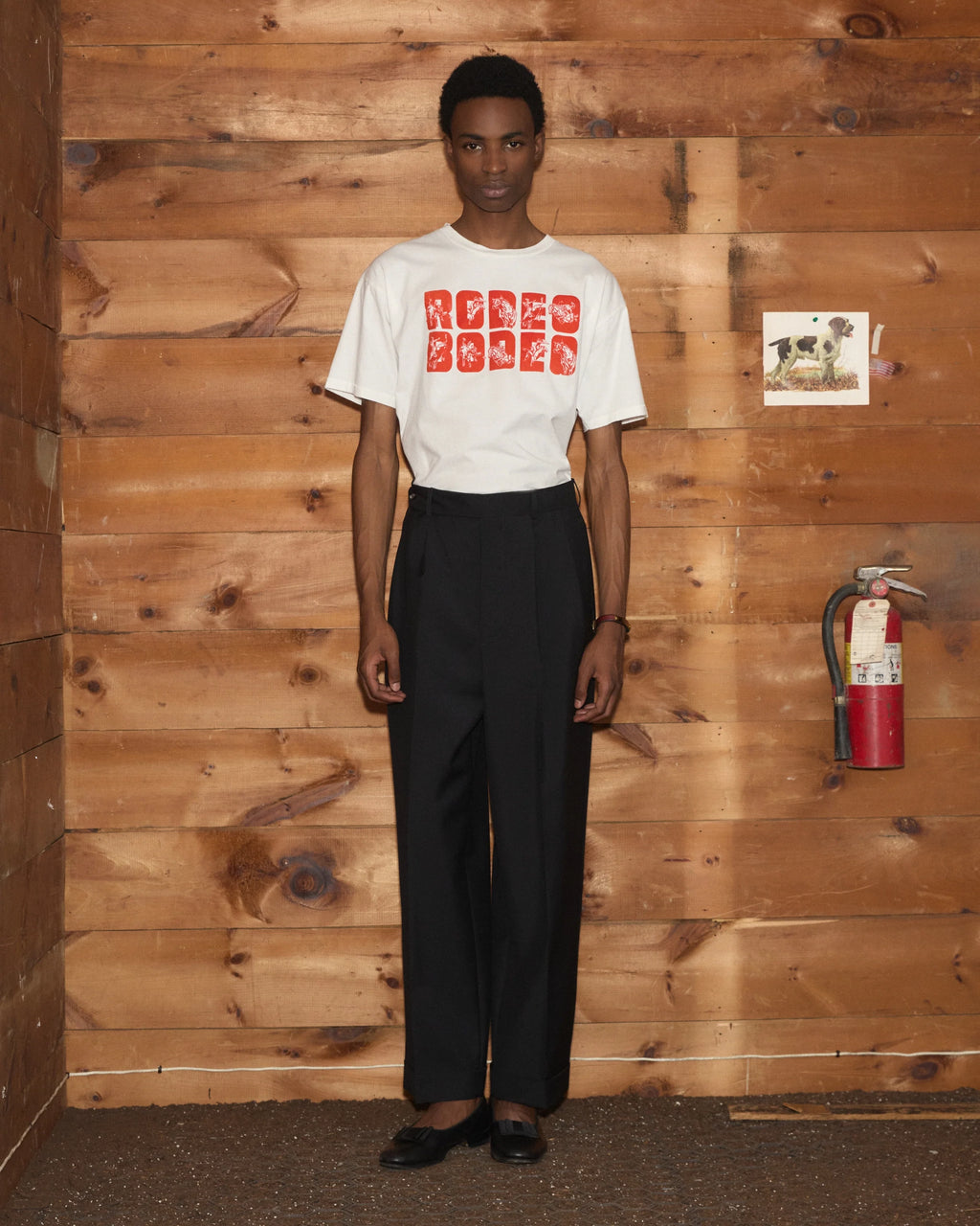 Model wearing Bode Rodeo Bodeo Tee in white with a red flocked graphic across the chest.
