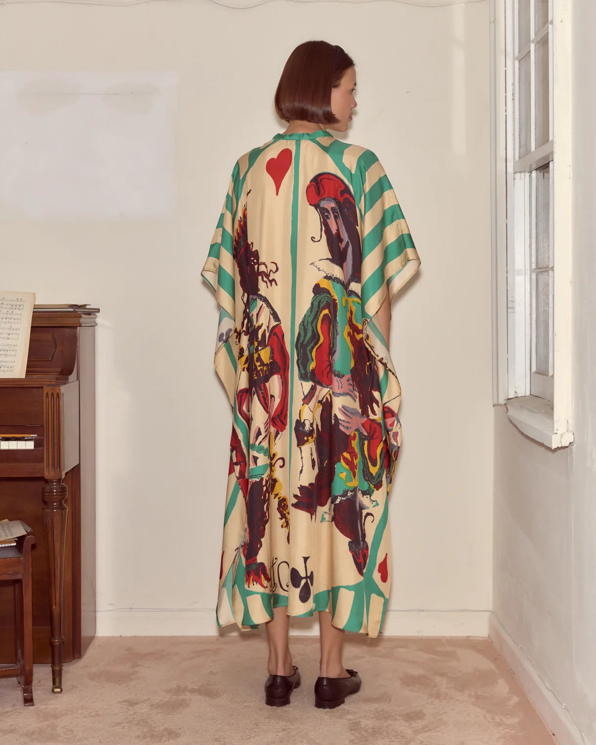 Person wearing a colorful patterned dress standing in a room with a piano.