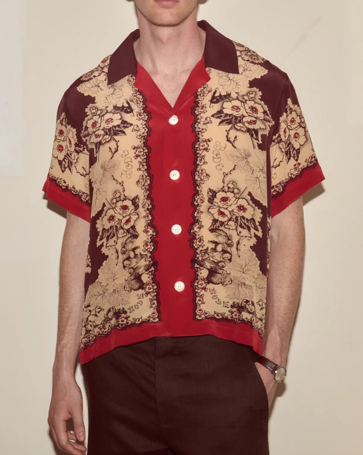 Person wearing a patterned shirt with red and brown colors on a plain background