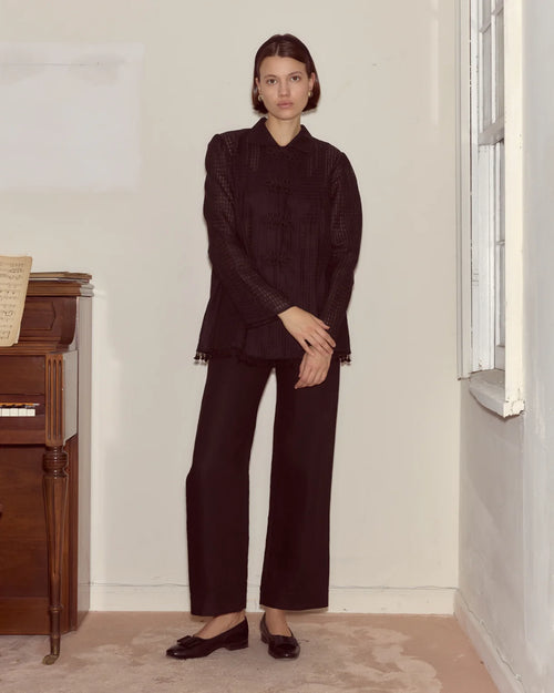 Woman wearing a dark outfit standing in a room with a wooden cabinet and window.