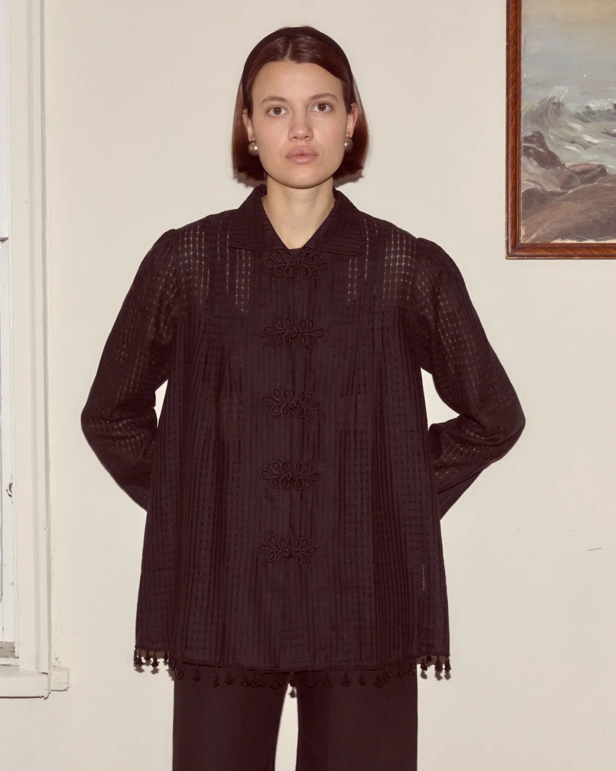 Person wearing a dark textured coat standing against a plain wall.