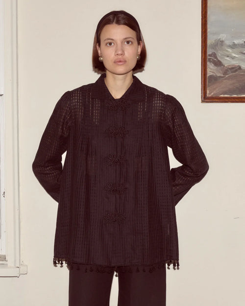 Person wearing a dark textured coat standing against a plain wall.