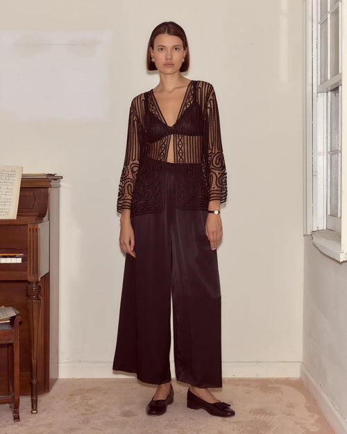 Woman wearing a sheer black top and wide-leg pants in a room with a piano.