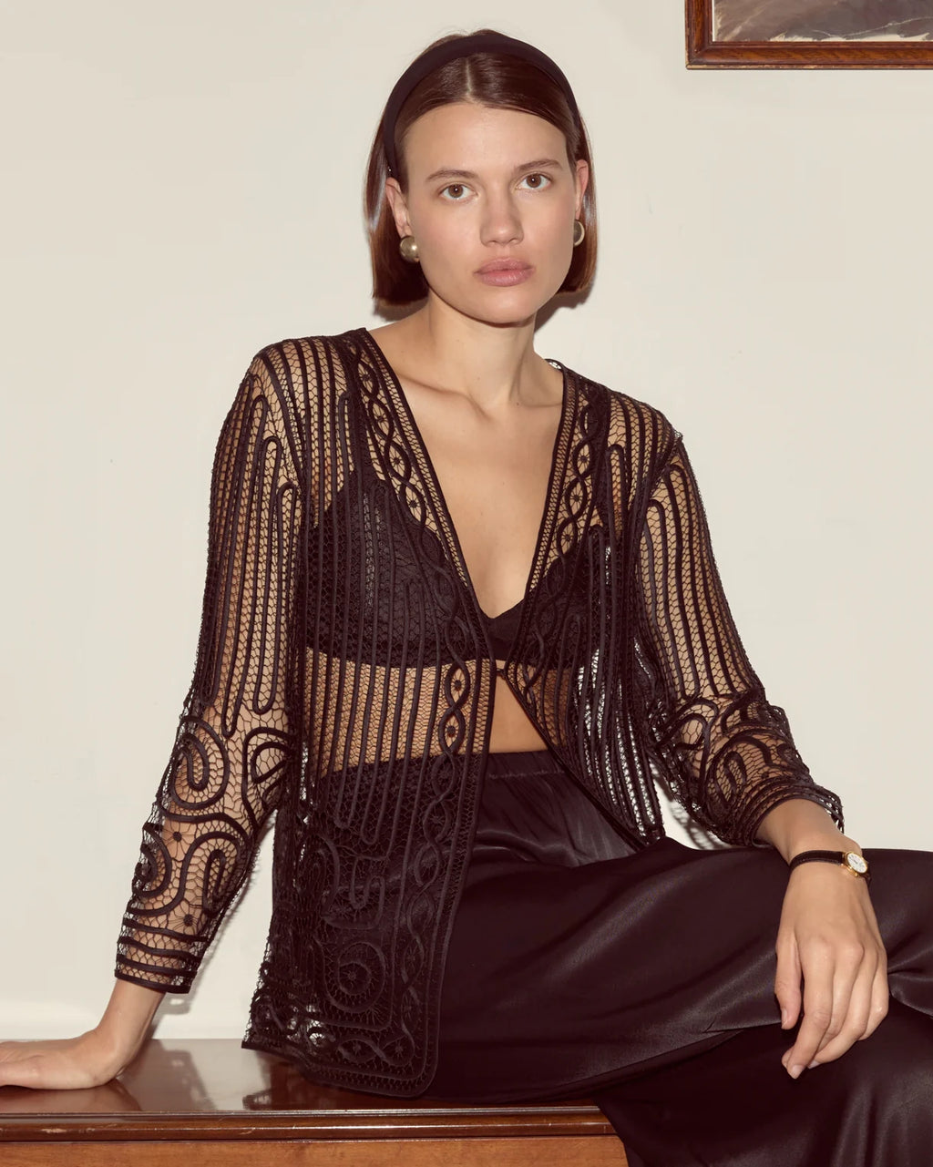 Woman wearing a black and gold patterned outfit sitting on a wooden surface.