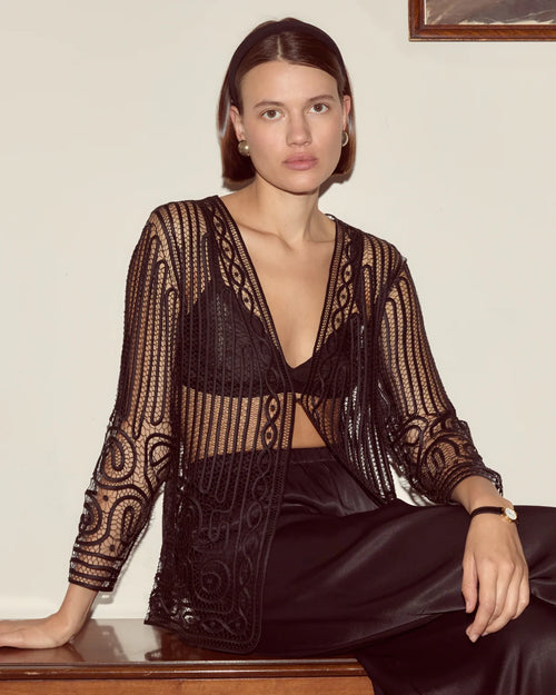 Woman wearing a black and gold patterned outfit sitting on a wooden surface.