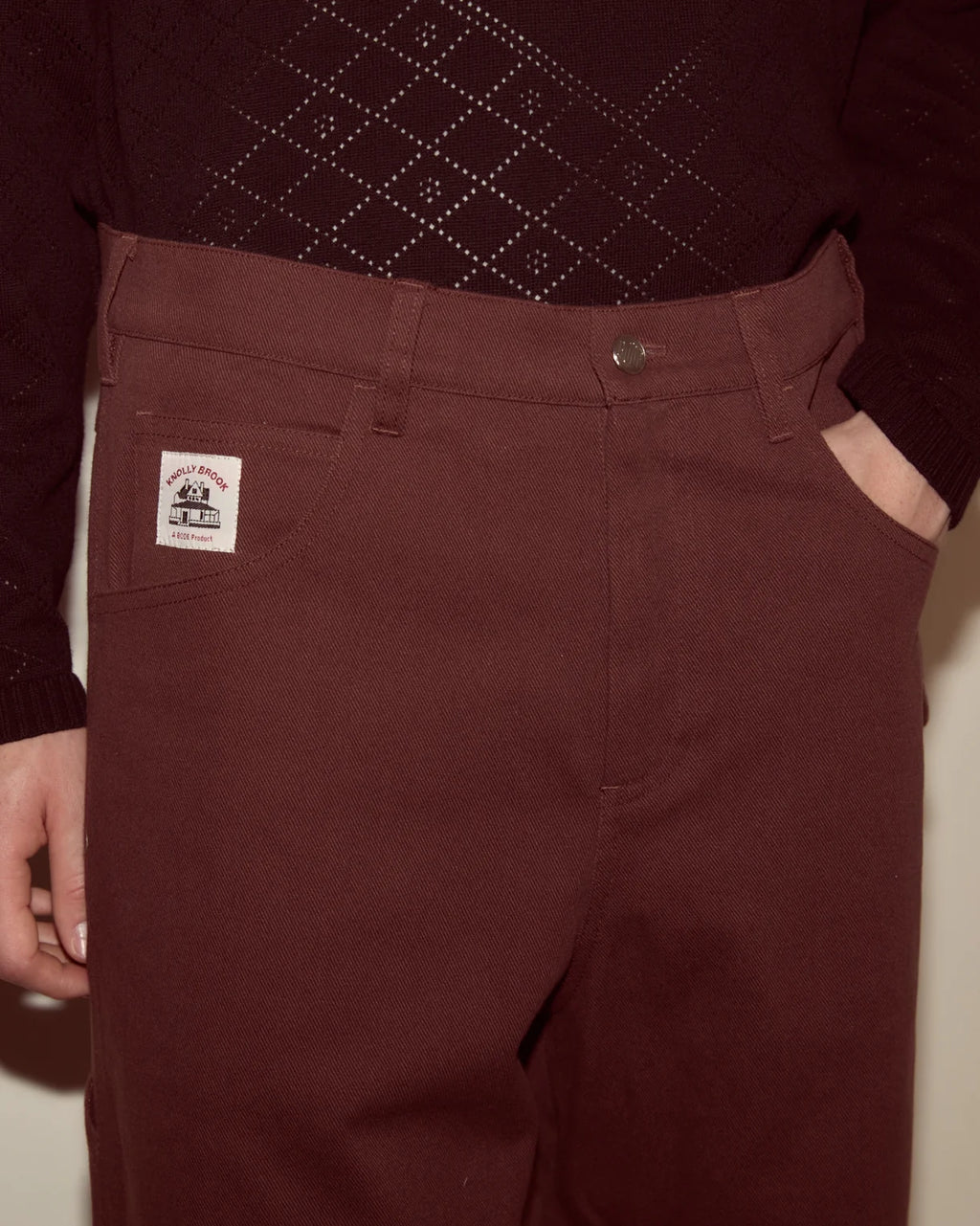 Maroon pants with a brand label worn by a person against a neutral background