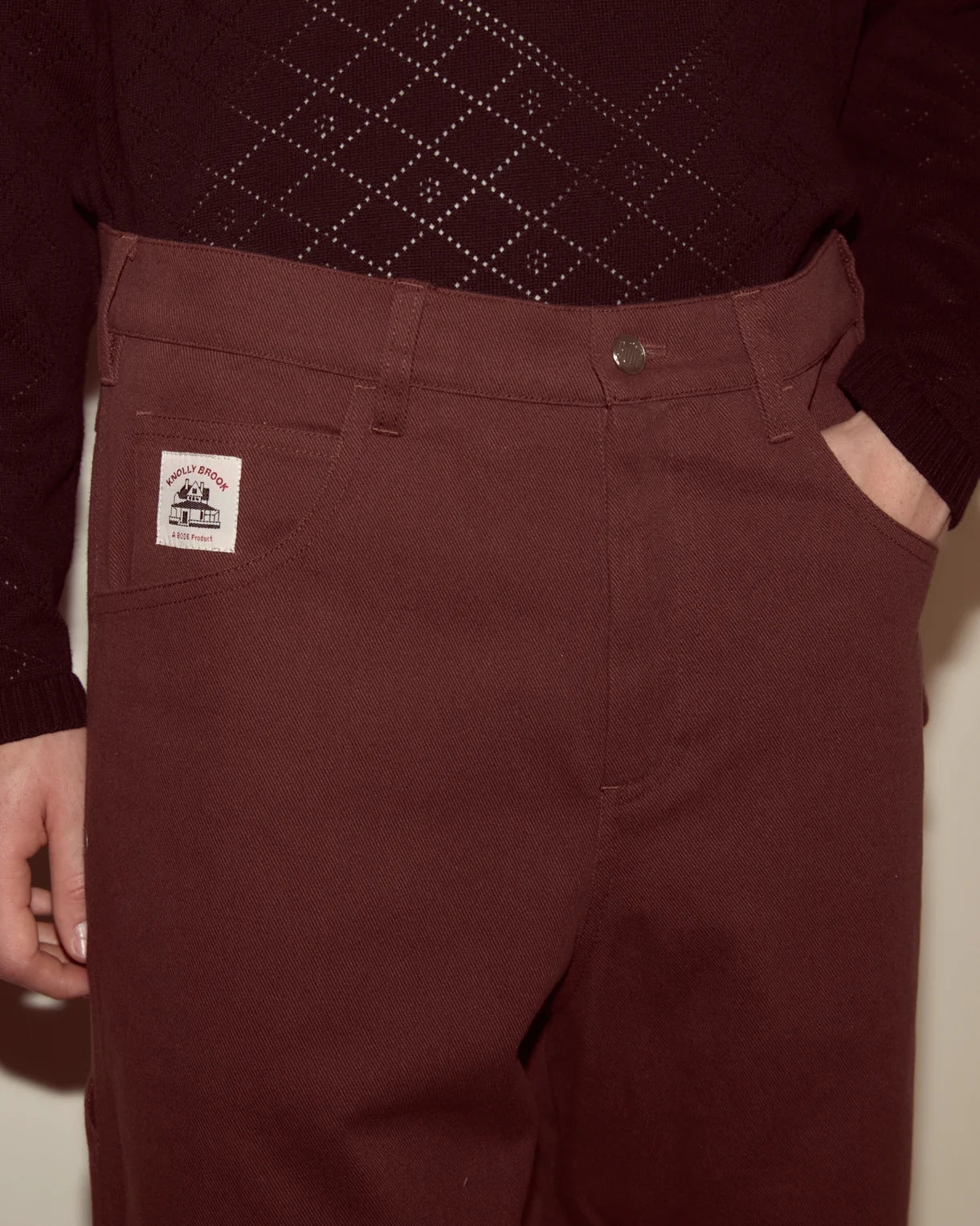 Maroon pants with a brand label worn by a person against a neutral background