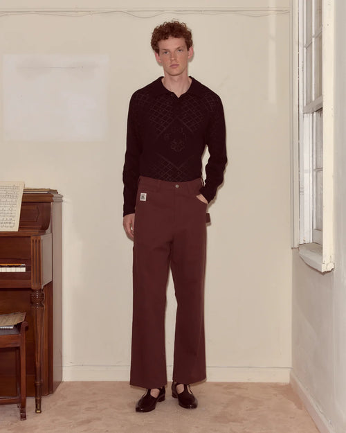 Man wearing a dark sweater and maroon pants standing in a room with a piano and window.