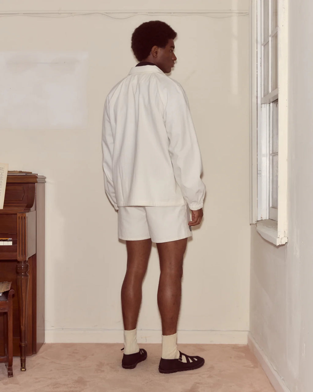 Person wearing a white outfit standing in a room with a piano.