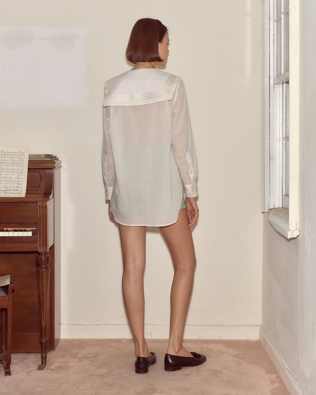 Model wearing white Bode cotton voile shirt with a sailor collar, chest patch pocket and antique pearl buttons.