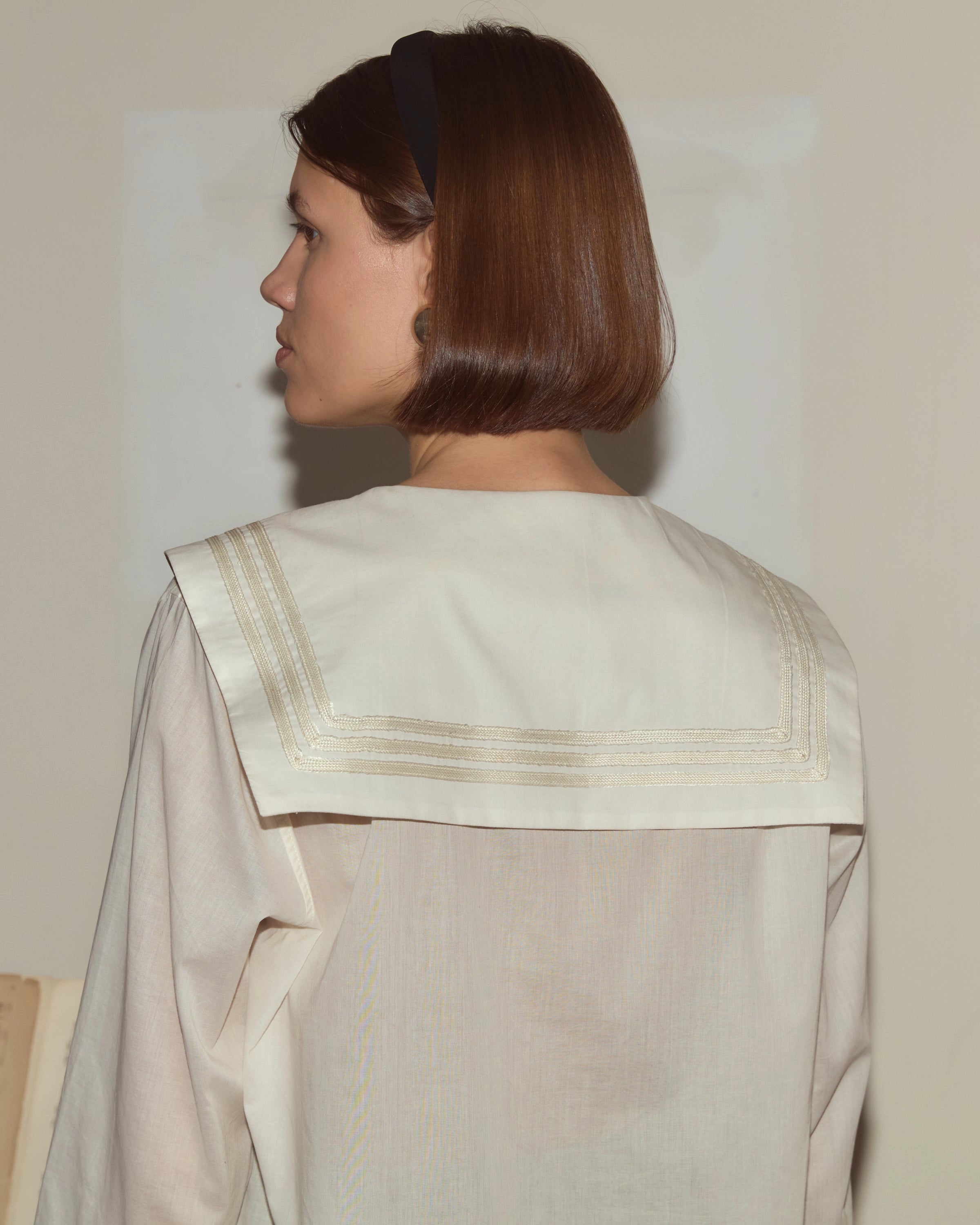 Model wearing white Bode cotton voile shirt with a sailor collar, chest patch pocket and antique pearl buttons.