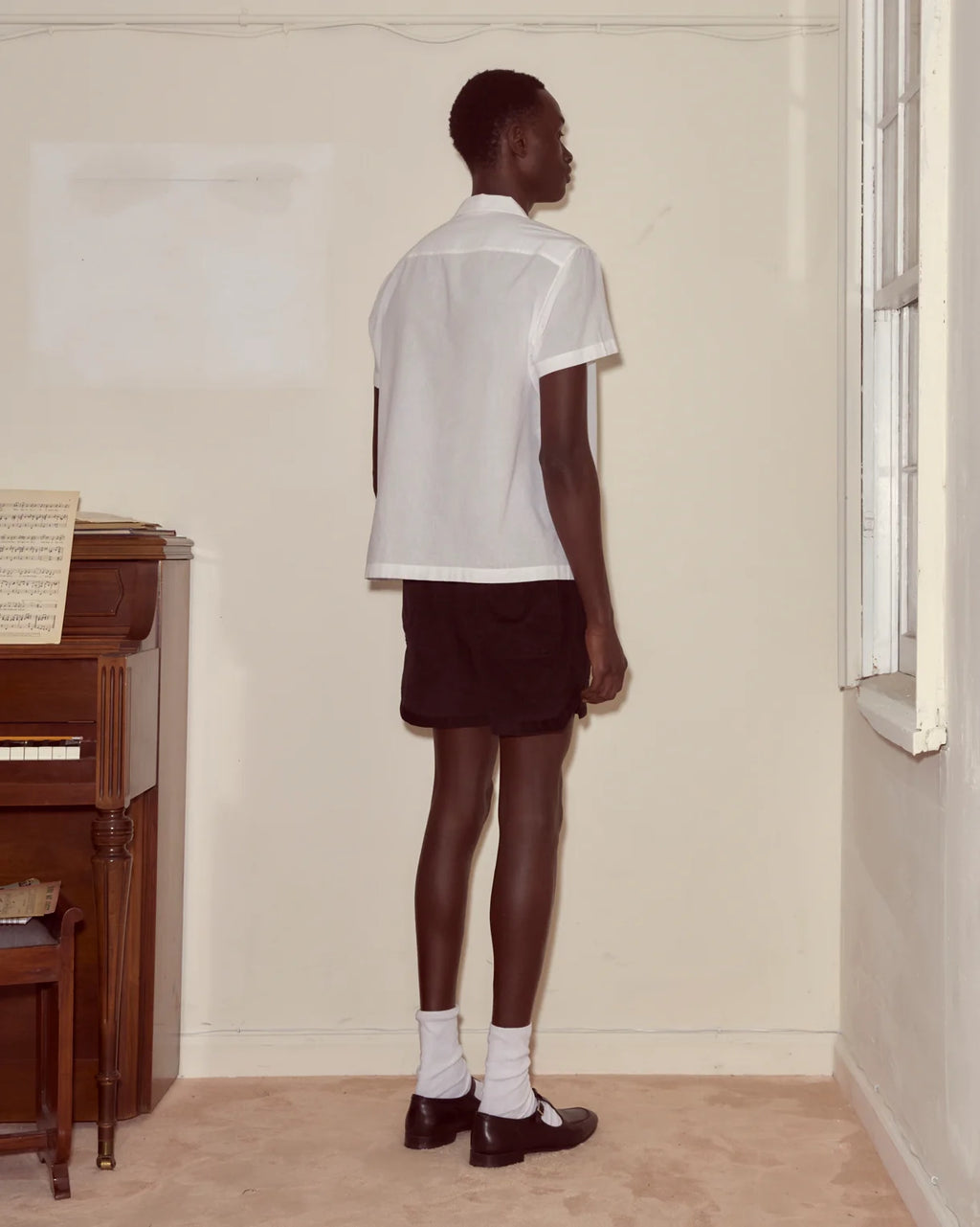 Person wearing a white shirt and black skirt standing in a room with a piano.
