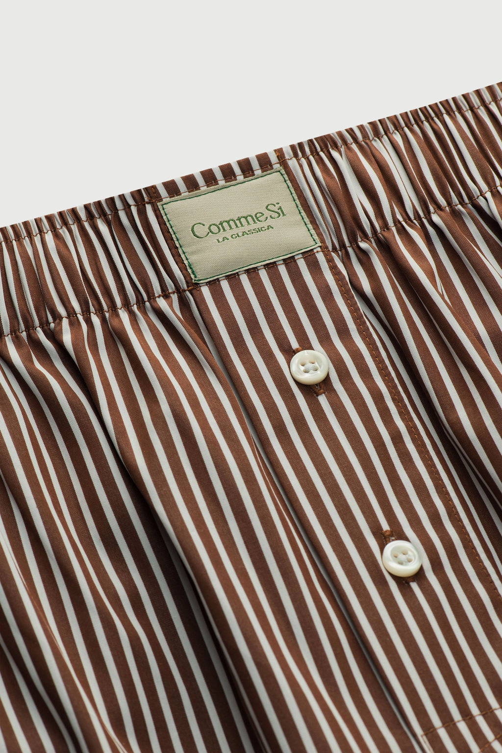 Close-up of brown and white striped pants with a visible brand label on a light background
