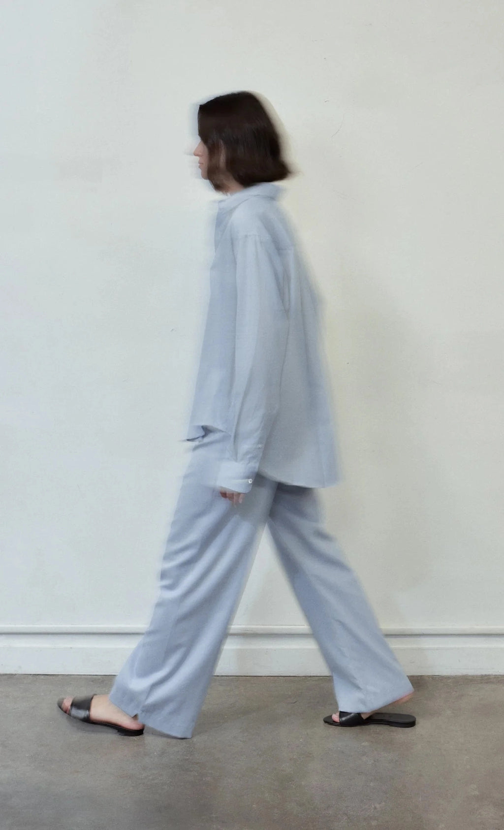Person wearing a light blue outfit standing against a plain white wall.