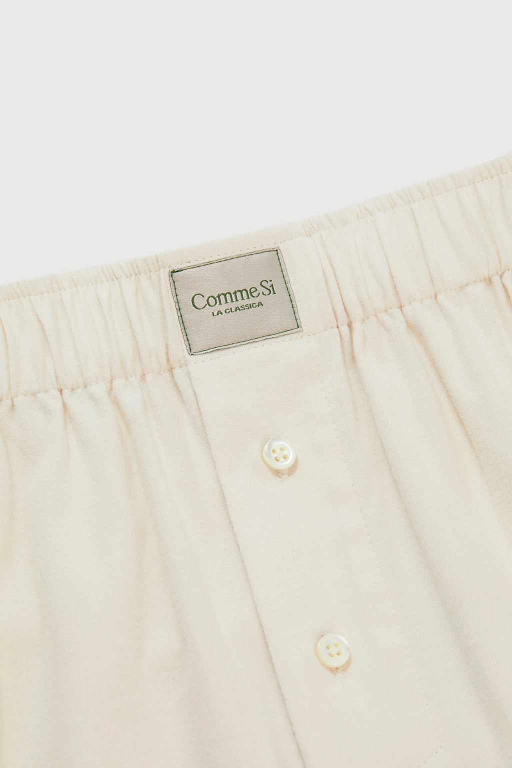 Close-up of beige pants with a brand label on a white background