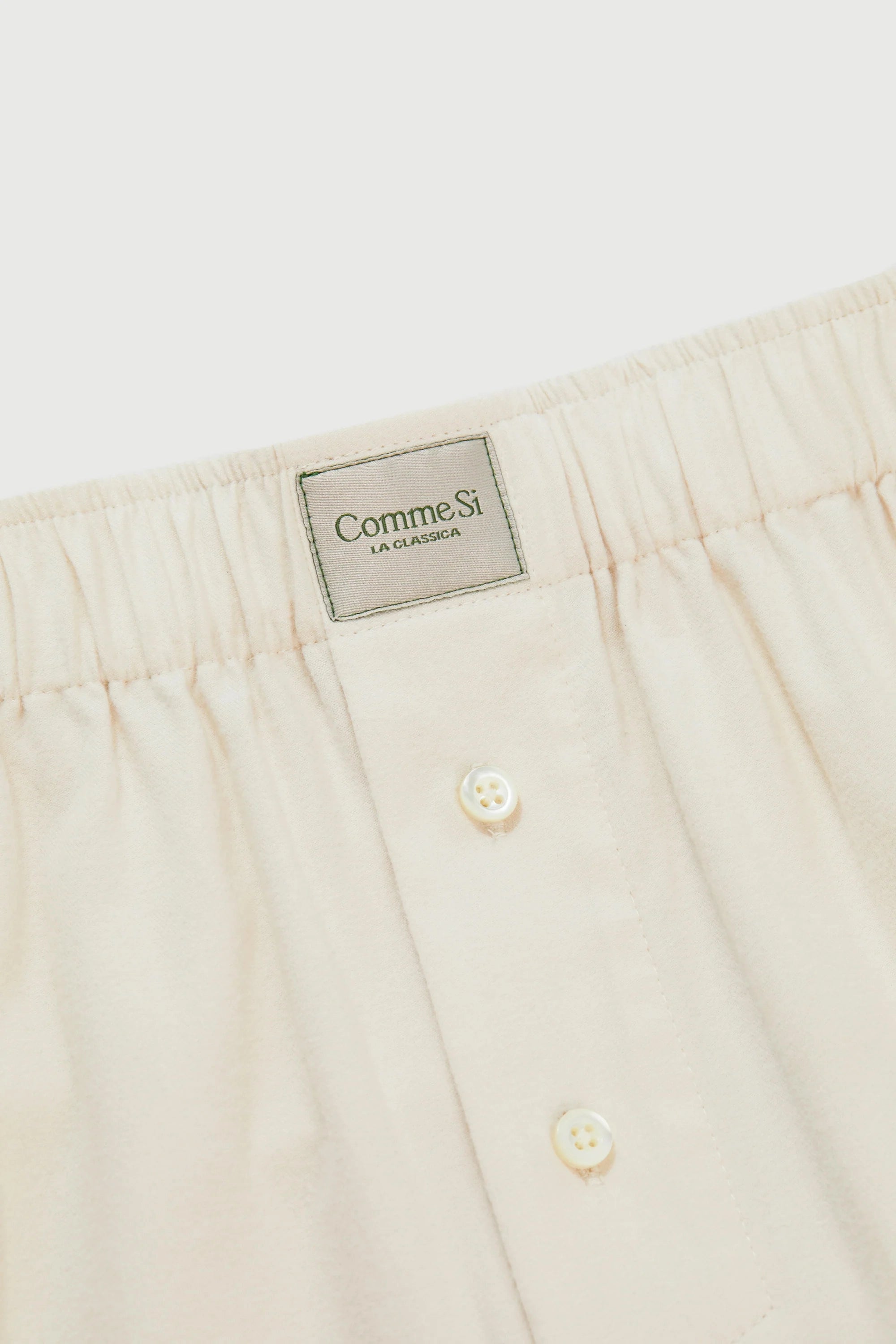 Close-up of beige pants with a brand label on a white background