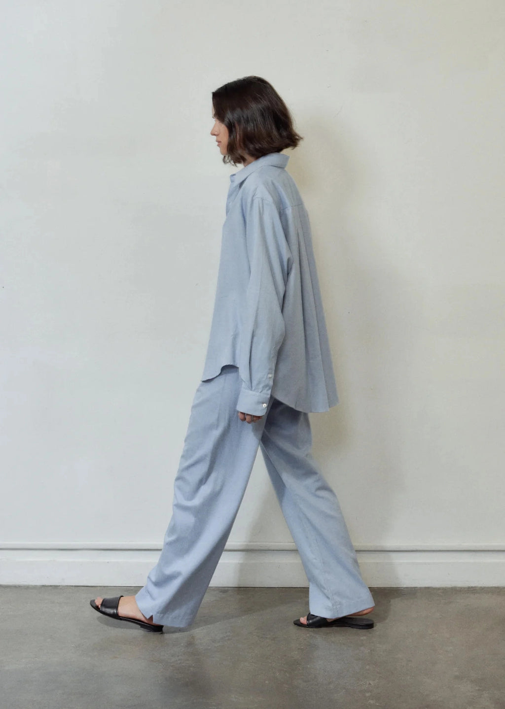 Person wearing a light blue outfit standing against a white wall.