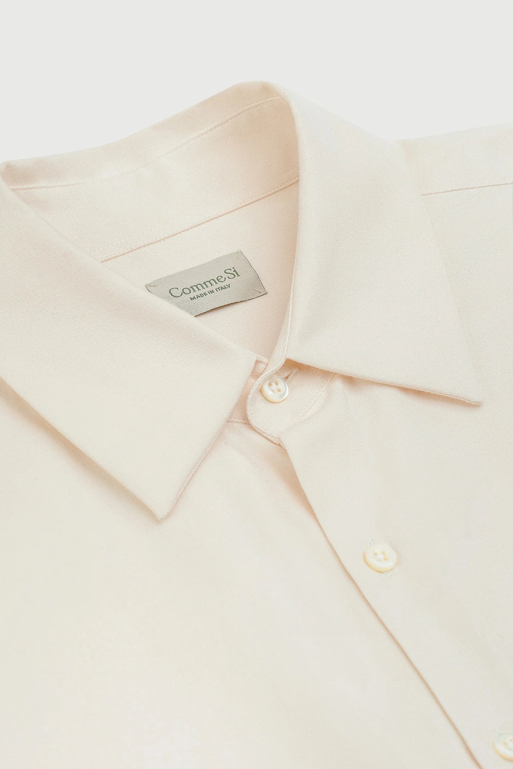 Close-up of a beige shirt with a Comme Si label on a white background