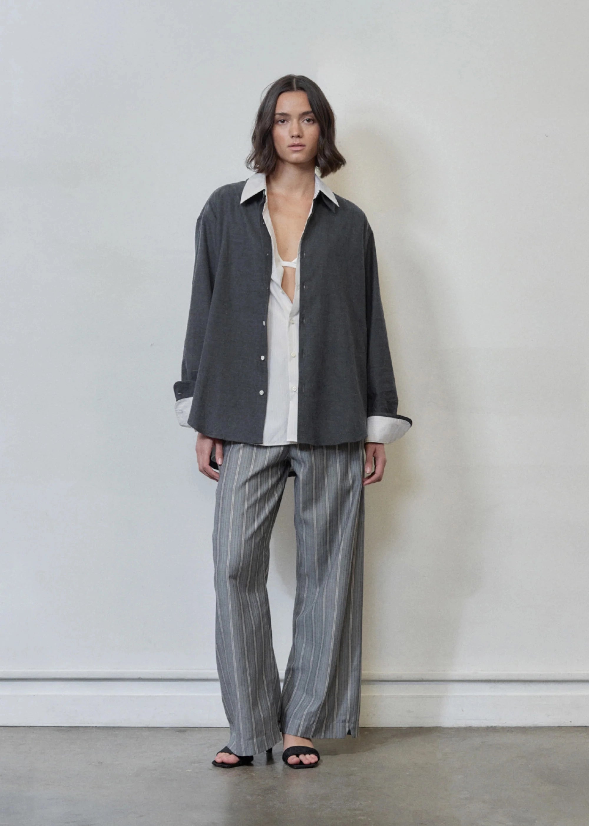 Person wearing a dark shirt over a white shirt with striped pants against a plain background