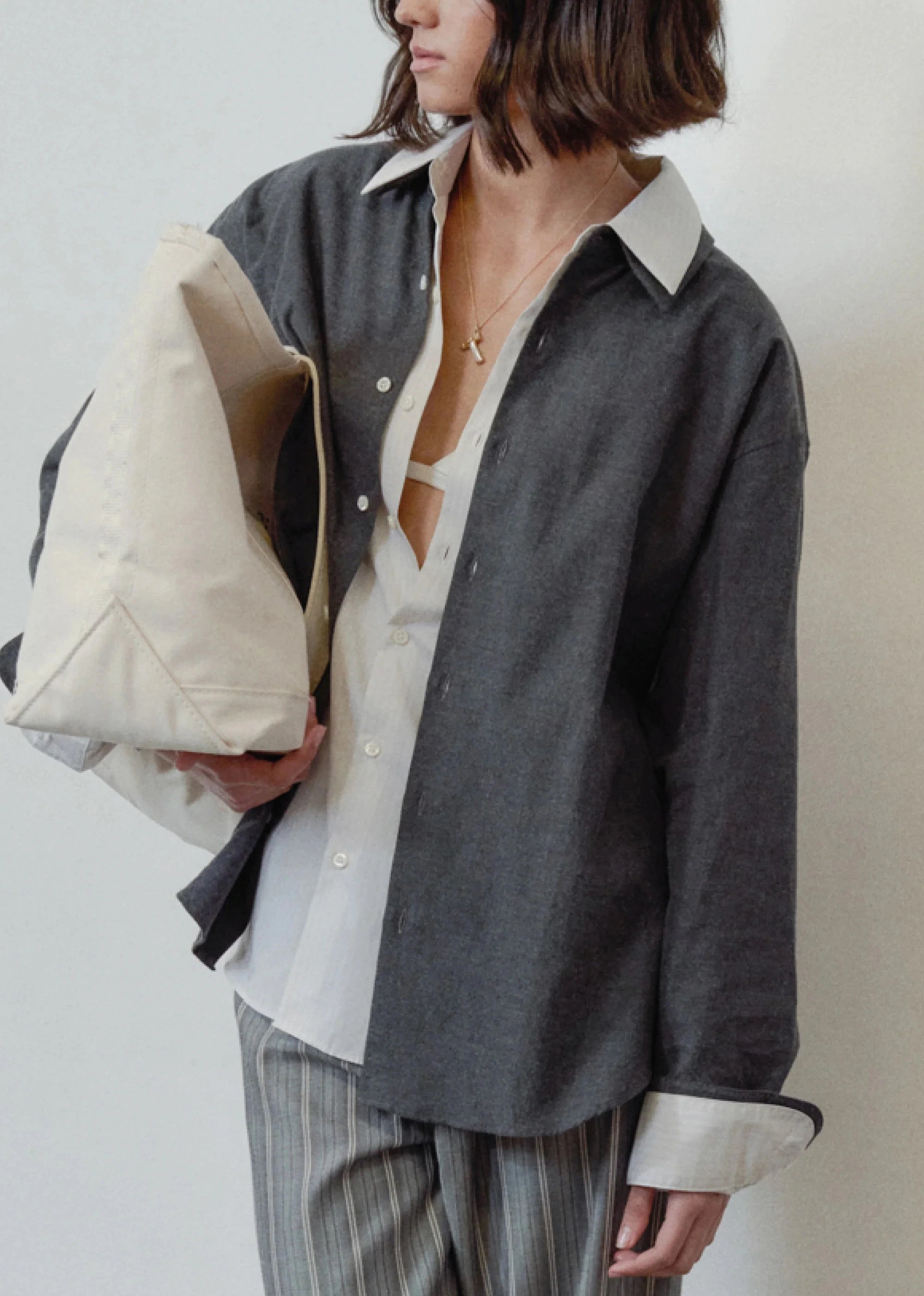 Person wearing a dark gray oversized shirt over a white shirt, holding a beige clutch.