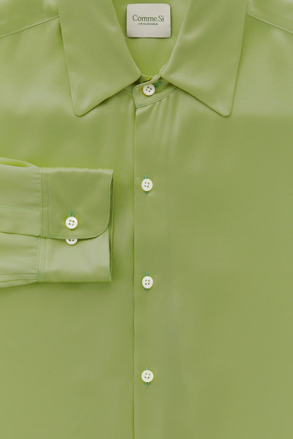 Close-up of a green shirt with buttons and a collar, featuring the Comme des Garçons brand label.