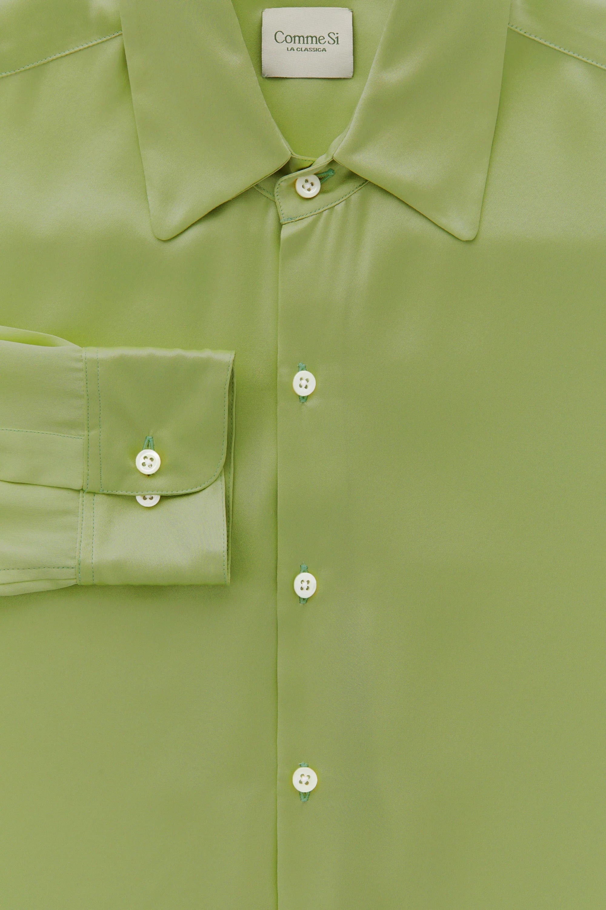 Close-up of a green shirt with buttons and a collar, featuring the Comme des Garçons brand label.