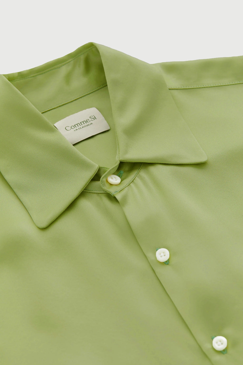 Close-up of a green shirt with a collar and buttons, featuring a brand label.