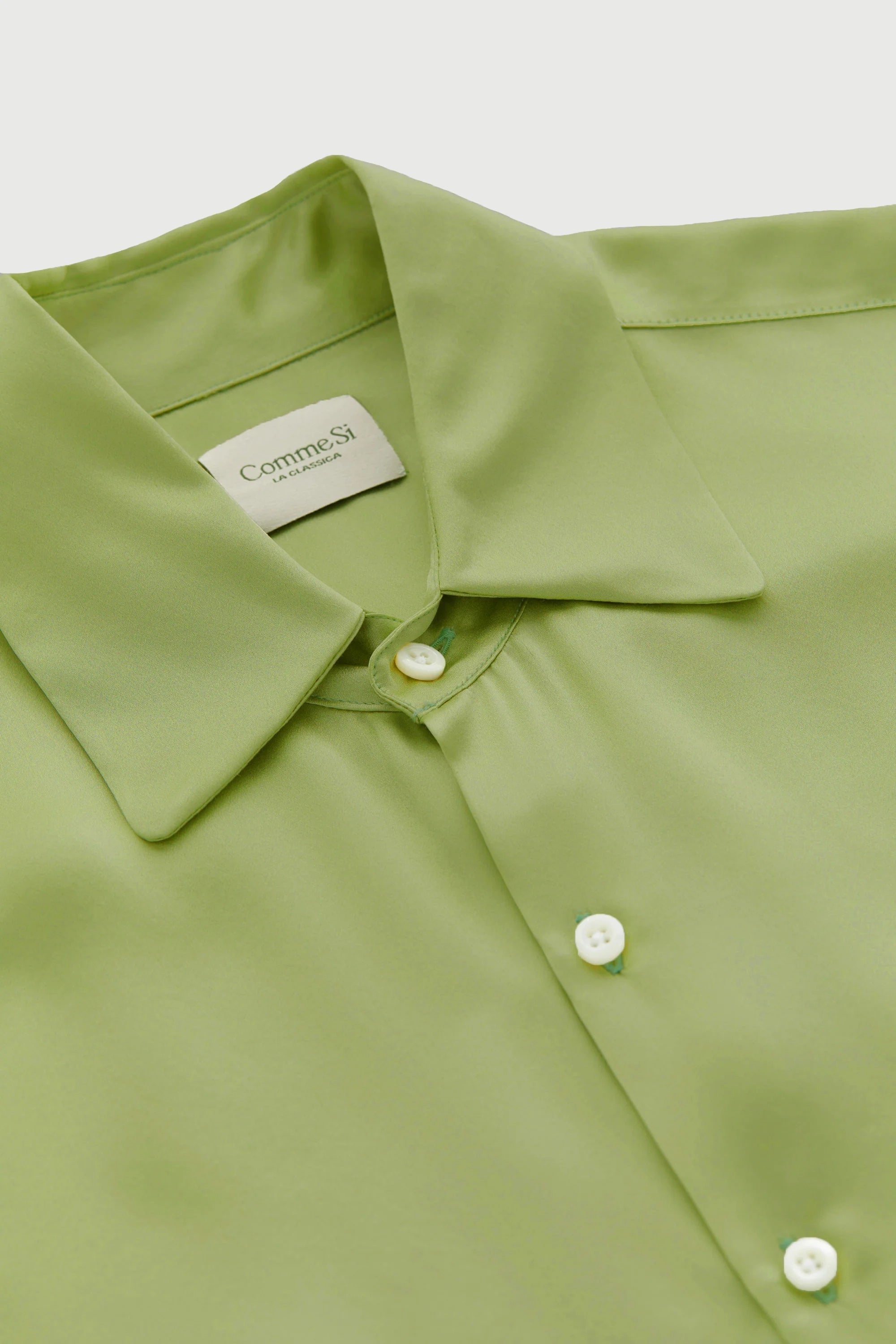 Close-up of a green shirt with a collar and buttons, featuring a brand label.