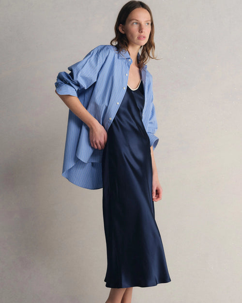 Model wearing Comme Si Silk Bias Slip Dress in Midnight under Comme Si La Shirt Classica in Celeste Stripe