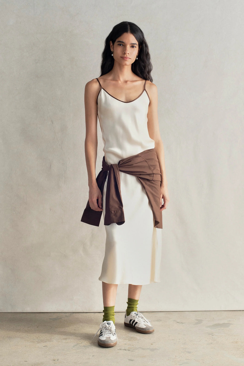 Woman wearing a white dress with a brown wrap over her shoulders against a plain background