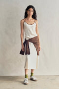 Woman wearing a white dress with a brown wrap over her shoulders against a plain background