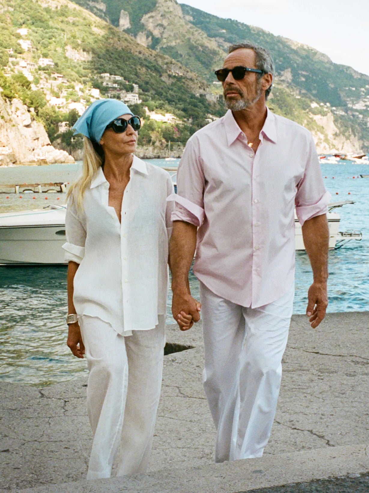 Man and woman walking along a coastal path wearing commesi with mountains and water in the background