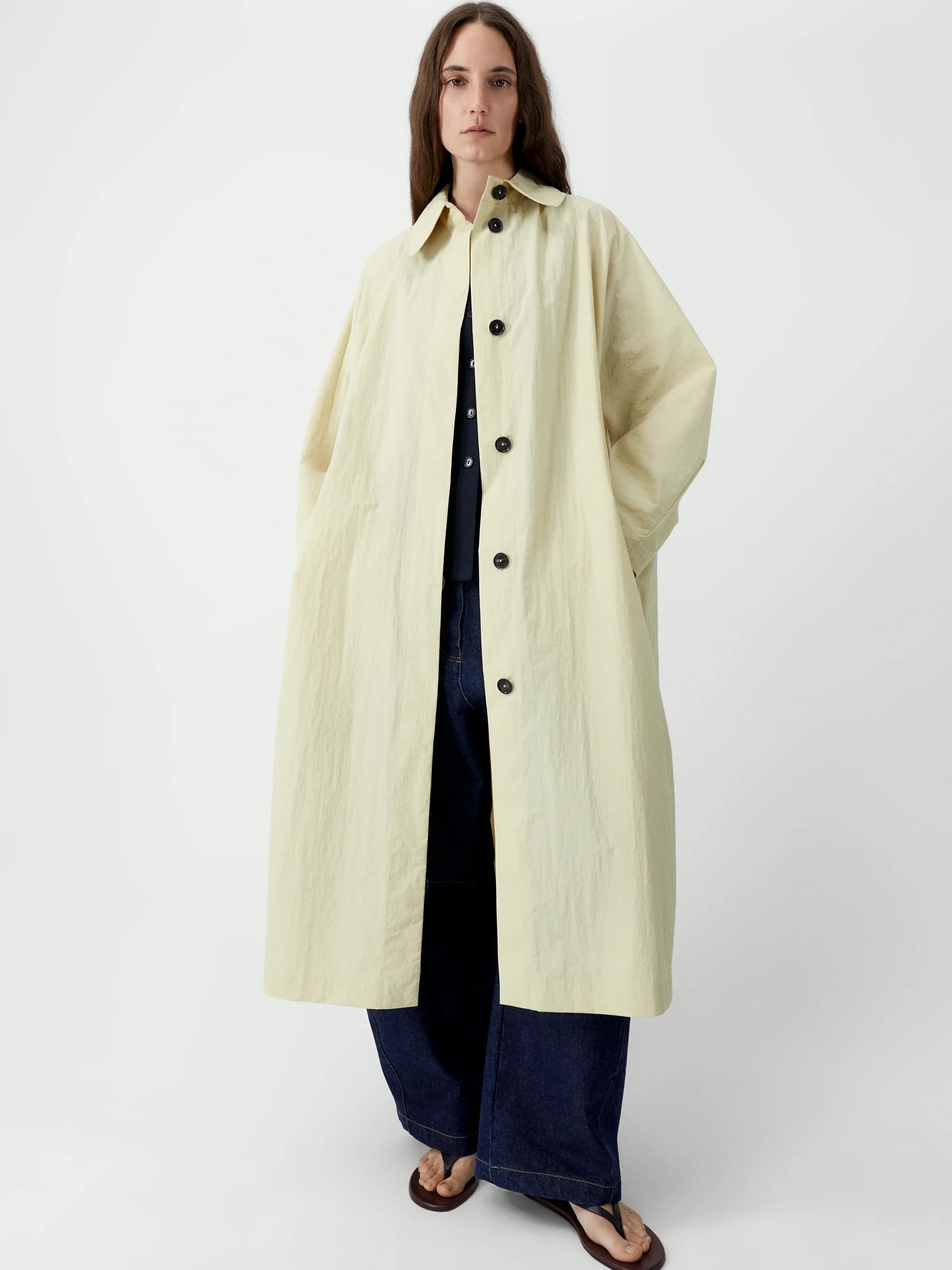 Woman wearing a long cream coat over a black outfit on a white background