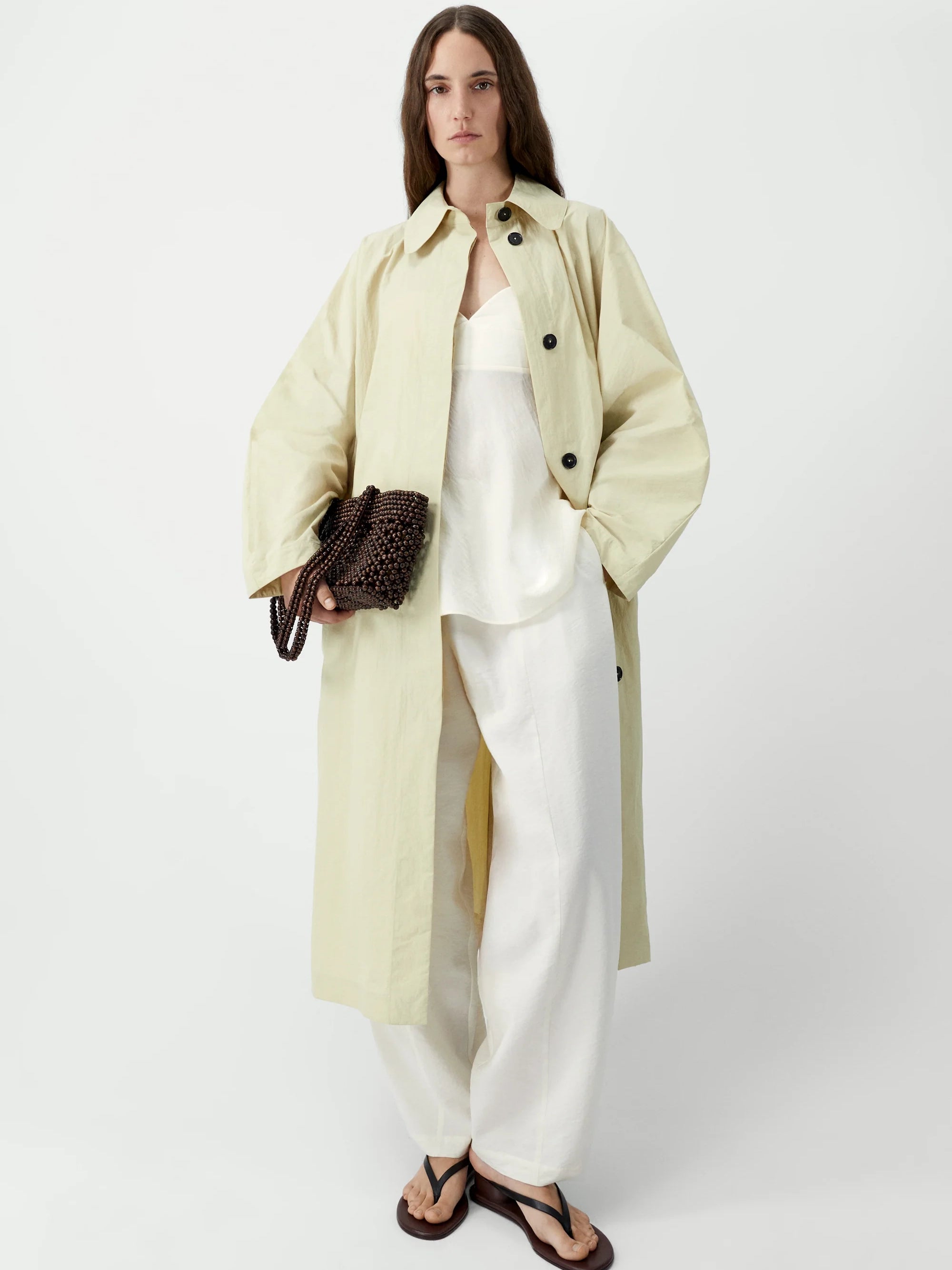 Woman wearing a light green coat over a white outfit on a white background