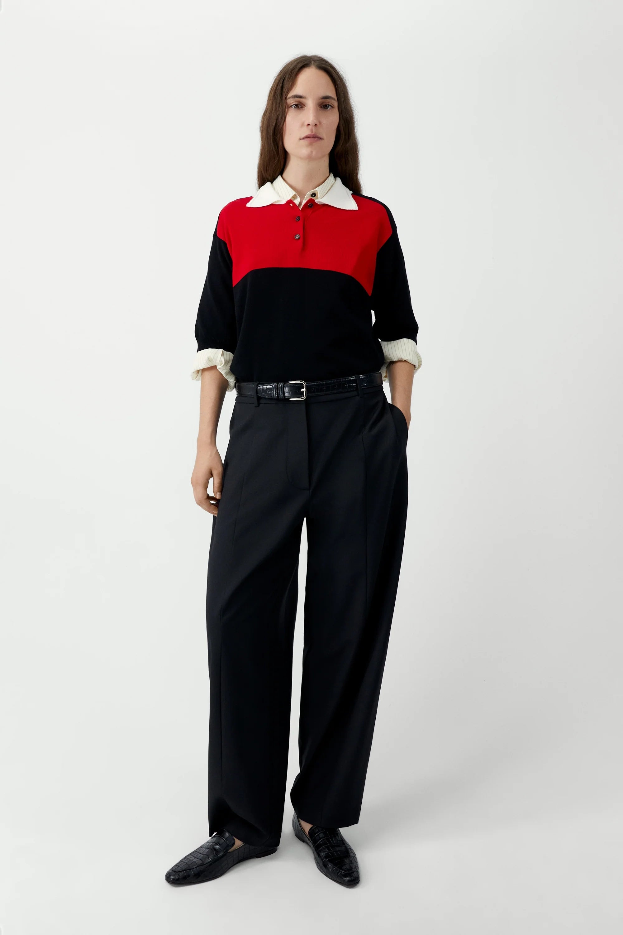 Person wearing a black and red color-blocked shirt with white collar and cuffs, paired with black pants on a white background.