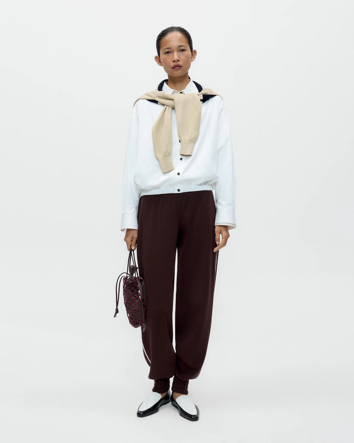 Model wearing CORDERA Organic Cotton Sporty Pants in brown with a contrasting white side stripe and gathered hems.