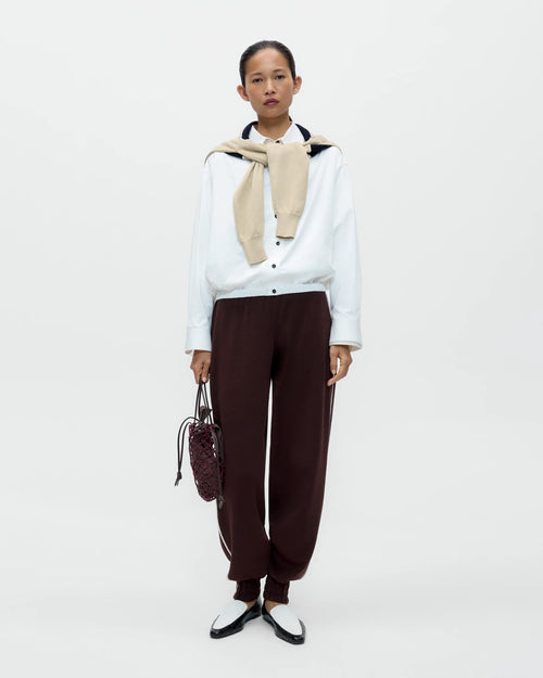 Model wearing CORDERA Organic Cotton Sporty Pants in brown with a contrasting white side stripe and gathered hems.