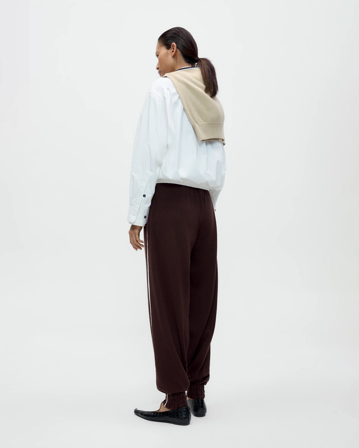 Model wearing CORDERA Organic Cotton Sporty Pants in brown with a contrasting white side stripe and gathered hems.