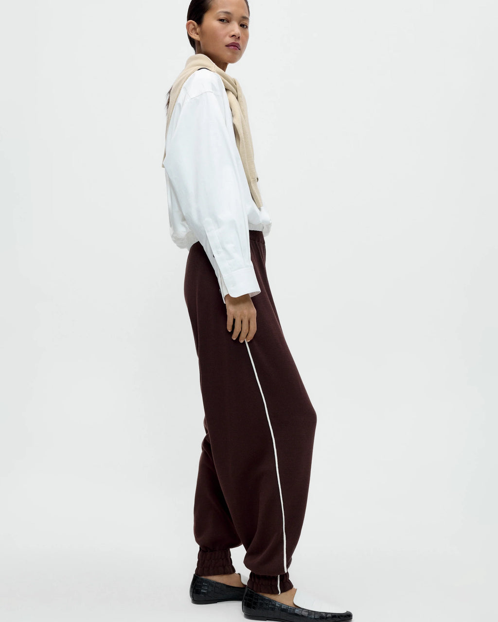 Model wearing CORDERA Organic Cotton Sporty Pants in brown with a contrasting white side stripe and gathered hems.