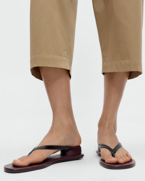 Model wearing CORDERA Estructura Sandal in black calfskin with slim black straps, brown-burgundy sole and raised oval heel.
